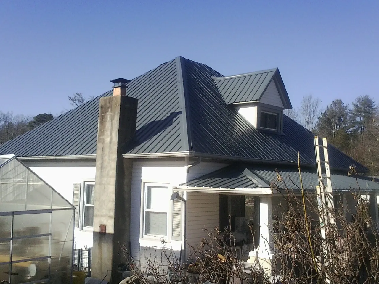 Dark blue standing seam metal roof on a white farmhouse with dormer — Slate & Tile Roof Repair by Roofing Brothers in East Lansing