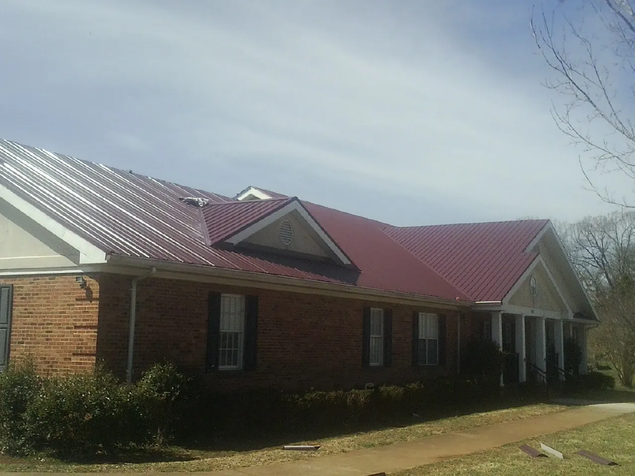 Red metal roof with gabled entries on a long brick building, from a Hail Damage Roof Repair job in East Lansing