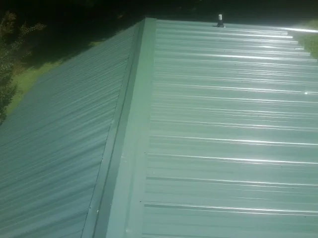 New green metal panels meeting at the ridge of a roof — Flat Roof Repair work by our crew in East Lansing