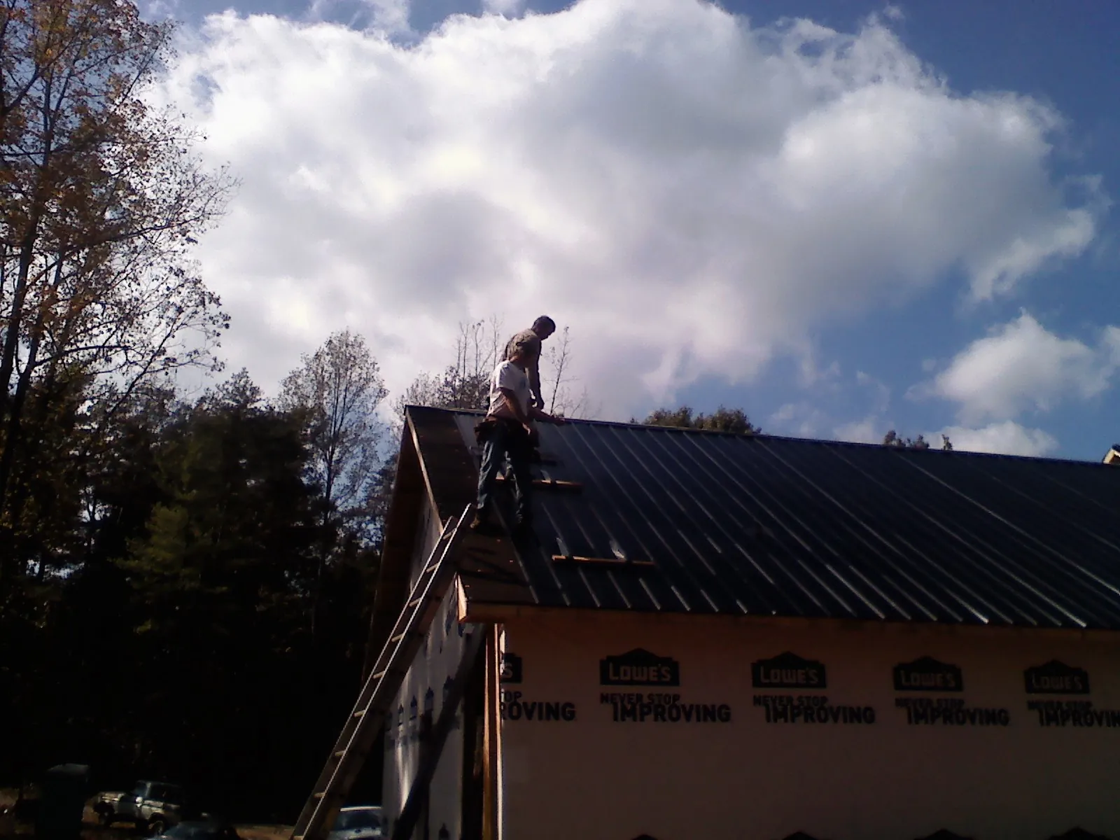 Roofer fastening dark metal panels high against a cloudy sky, from a Roof Inspection job in East Lansing