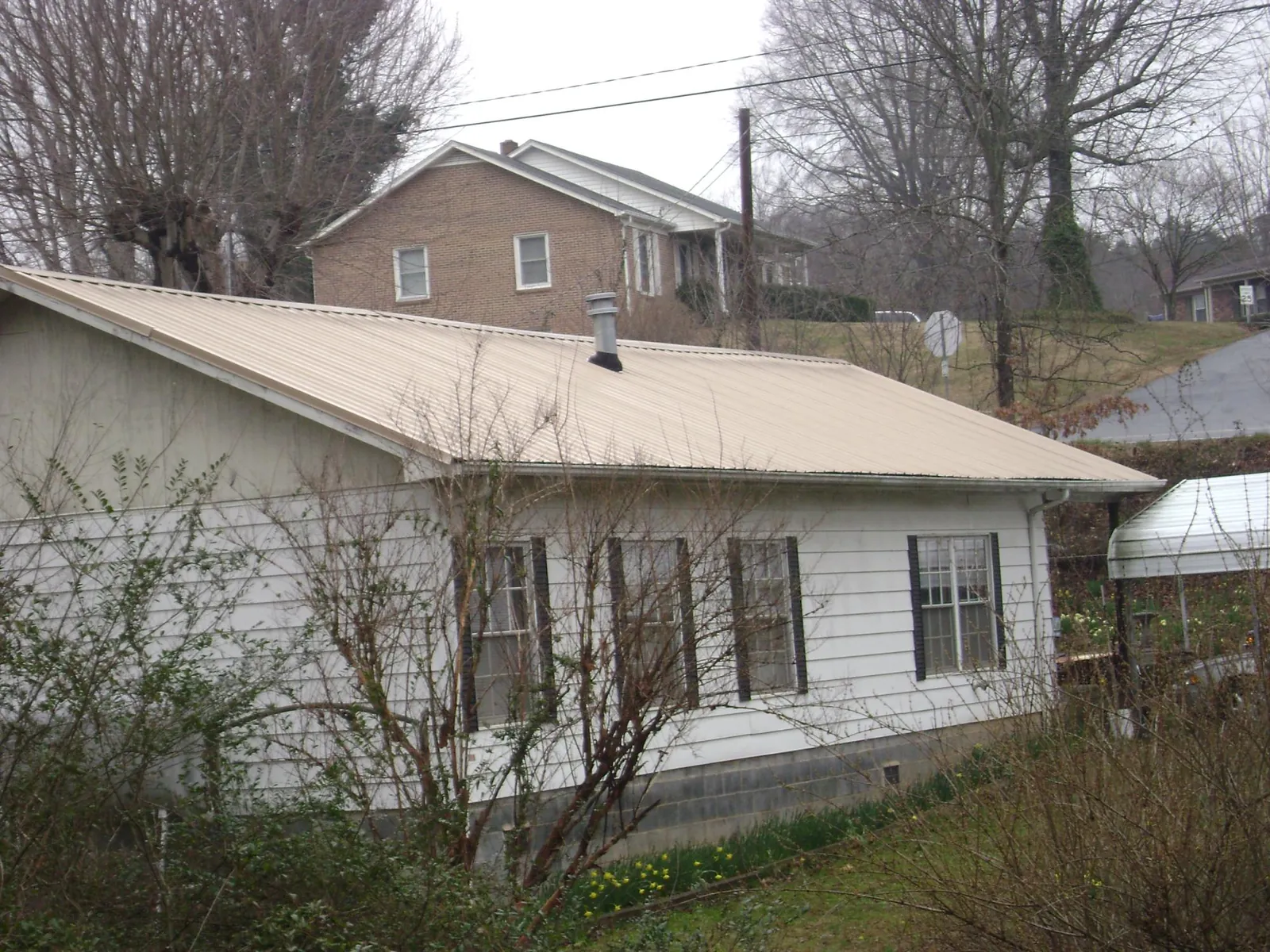 Tan metal roof on a white sided house set into a hillside — Commercial Roofing by Roofing Brothers in East Lansing